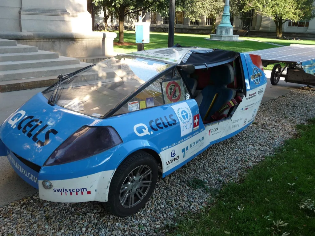 The blue-and-white Solartaxi three-wheeler parked in front of a building at MIT
