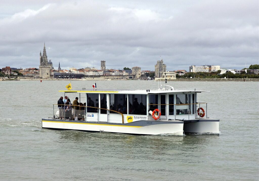 An electro-solar sea bus in front of the towers of La Rochelle's Old Port.
