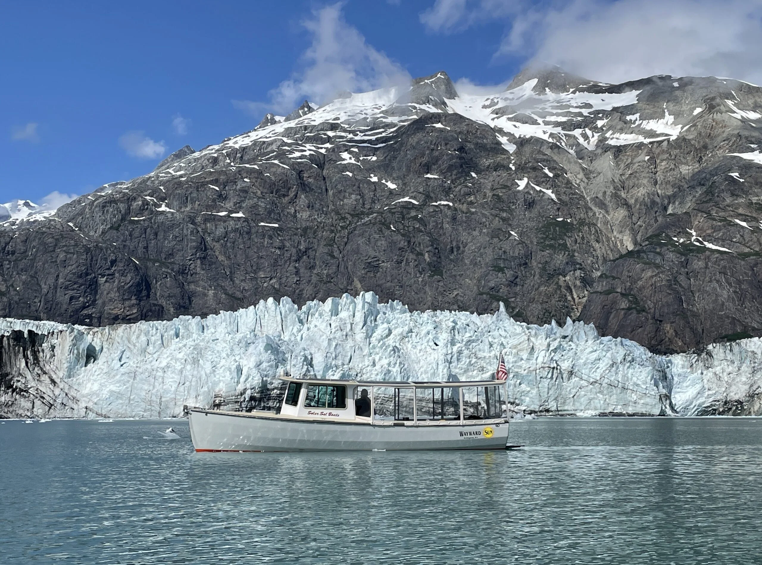 The small wooden solar boat Wayward Sun in front of a glacier in Glacier Bay, Alaska