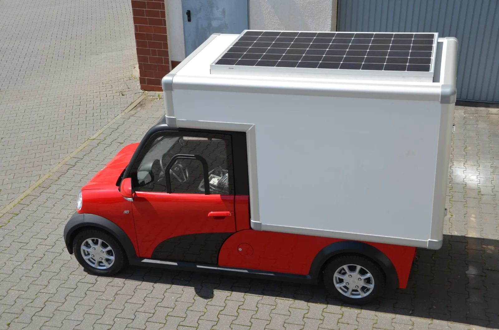 A small red ARI 458 electric micro-van with a white box body and solar panel on the roof