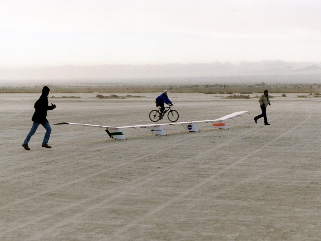 Crew members jog and cycle beside the quarter-scale model of Centurion in 1997.