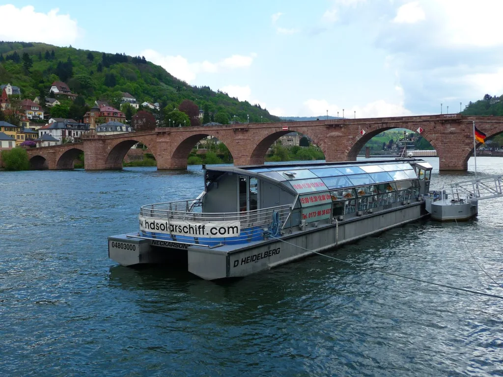The solar ship Neckarsonne on the Neckar in Heidelberg with the old bridge behind