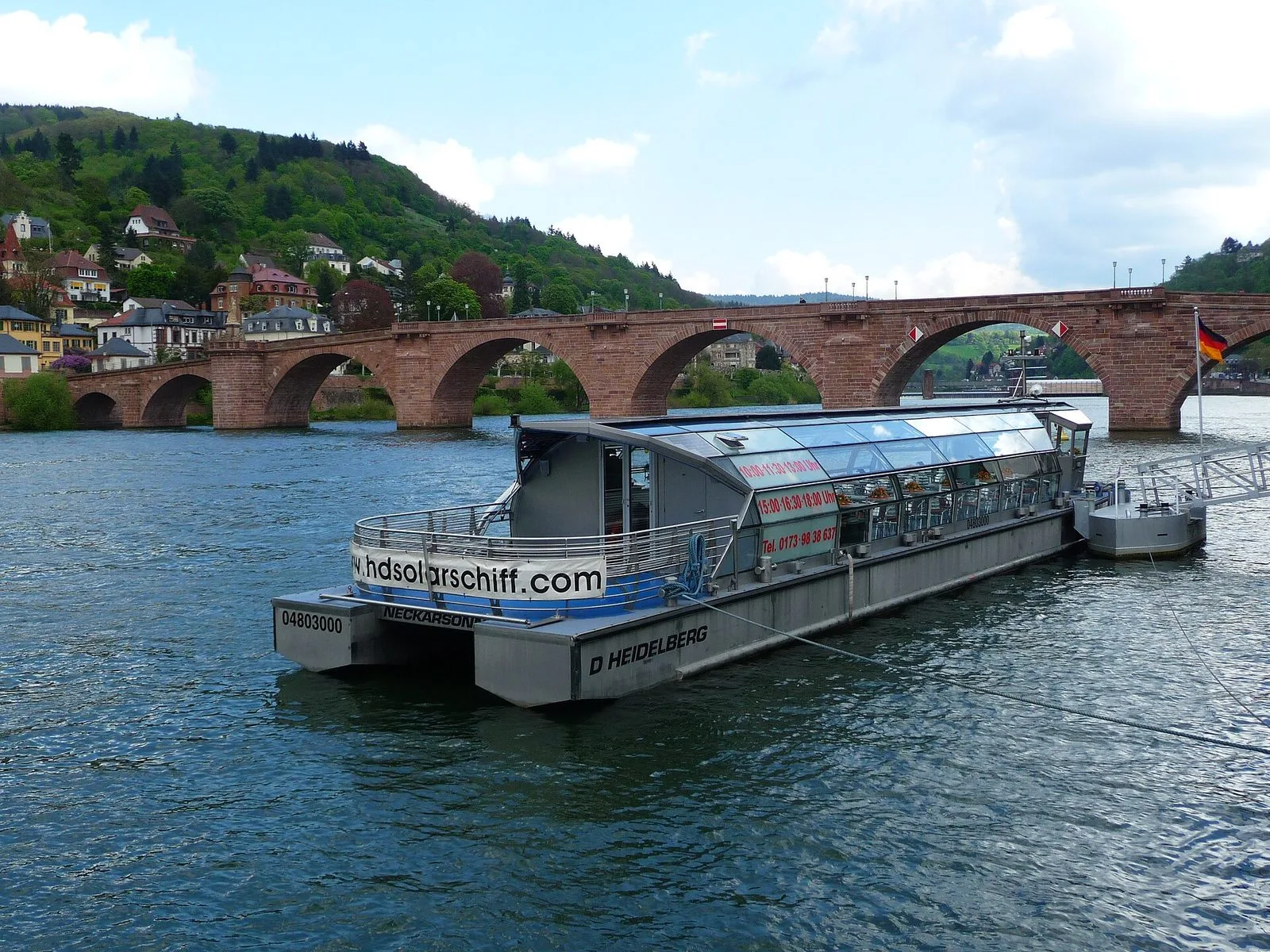 The solar ship Neckarsonne on the Neckar in Heidelberg with the old bridge behind