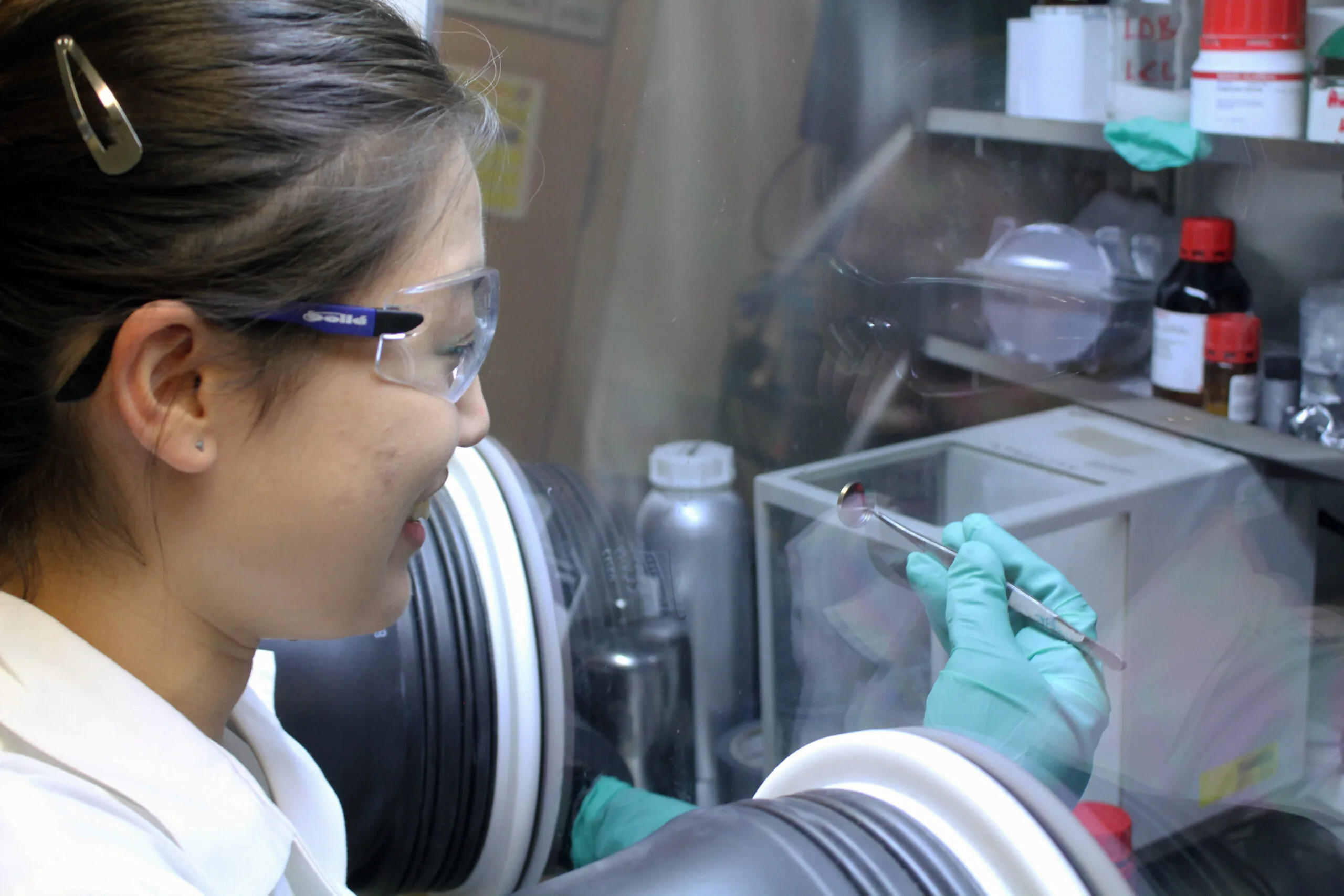 Researcher handling a small battery inside a sealed laboratory glovebox