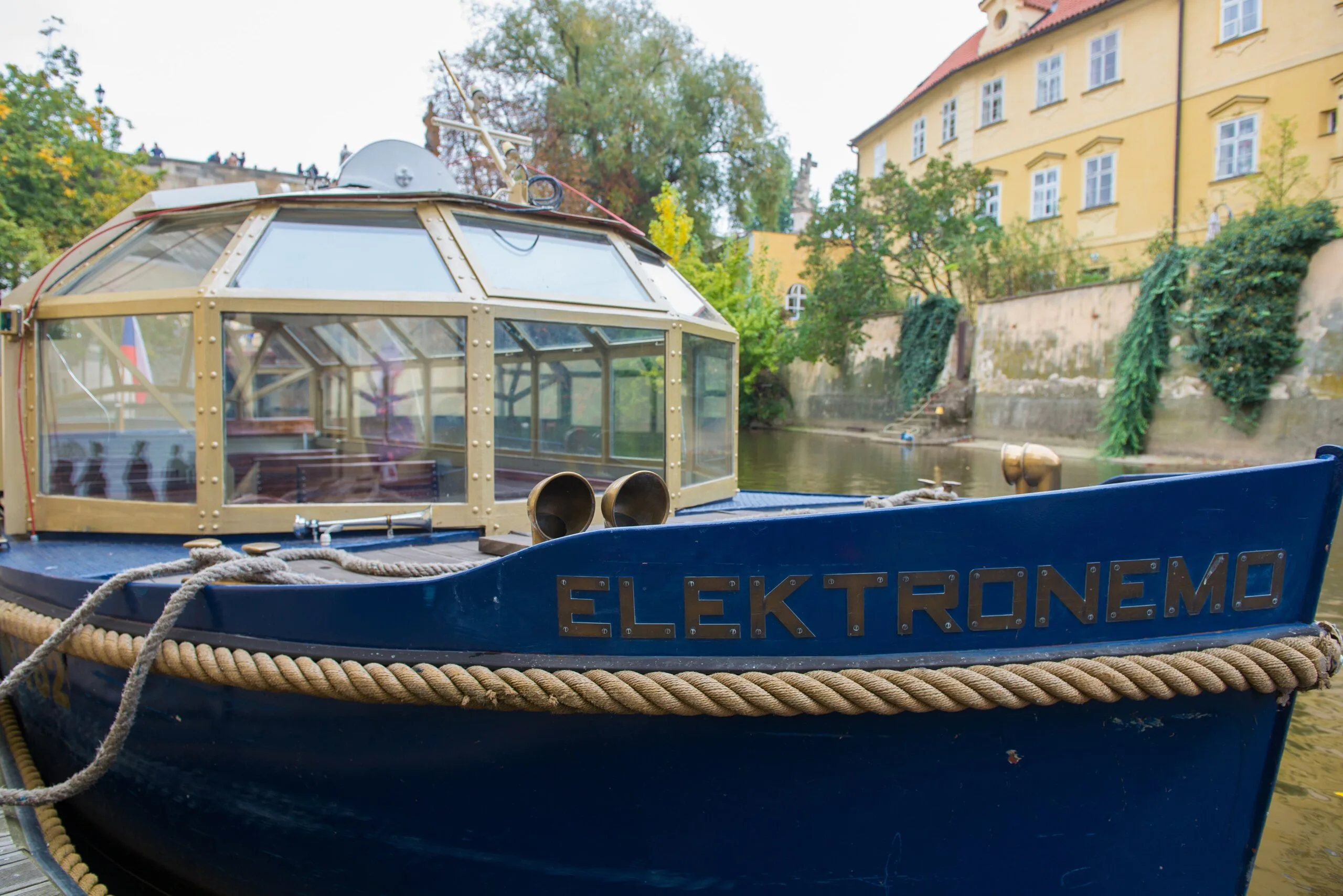 The blue solar boat Elektronemo with its glass cabin in the narrow Čertovka channel in Prague
