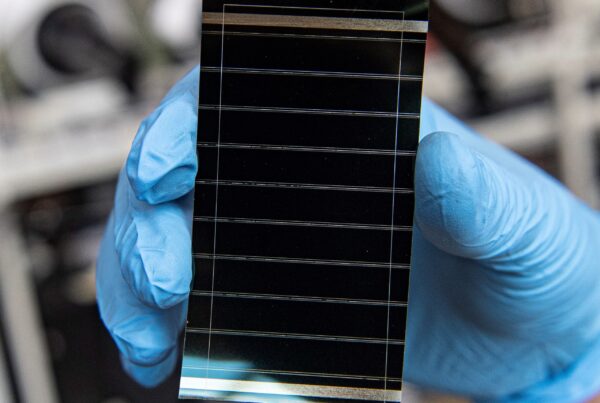 Researcher in blue gloves holding a perovskite solar cell