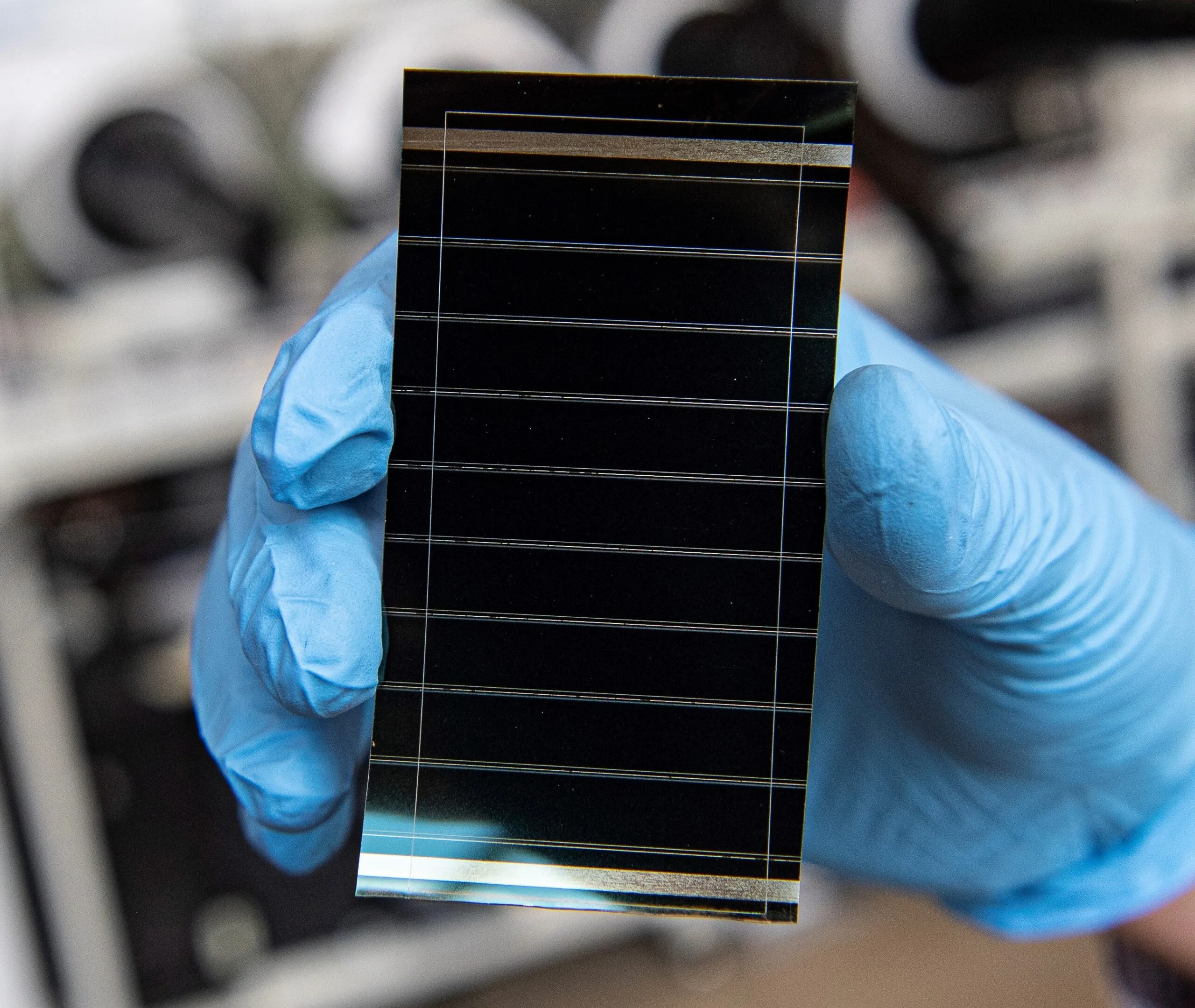 Researcher in blue gloves holding a perovskite solar cell