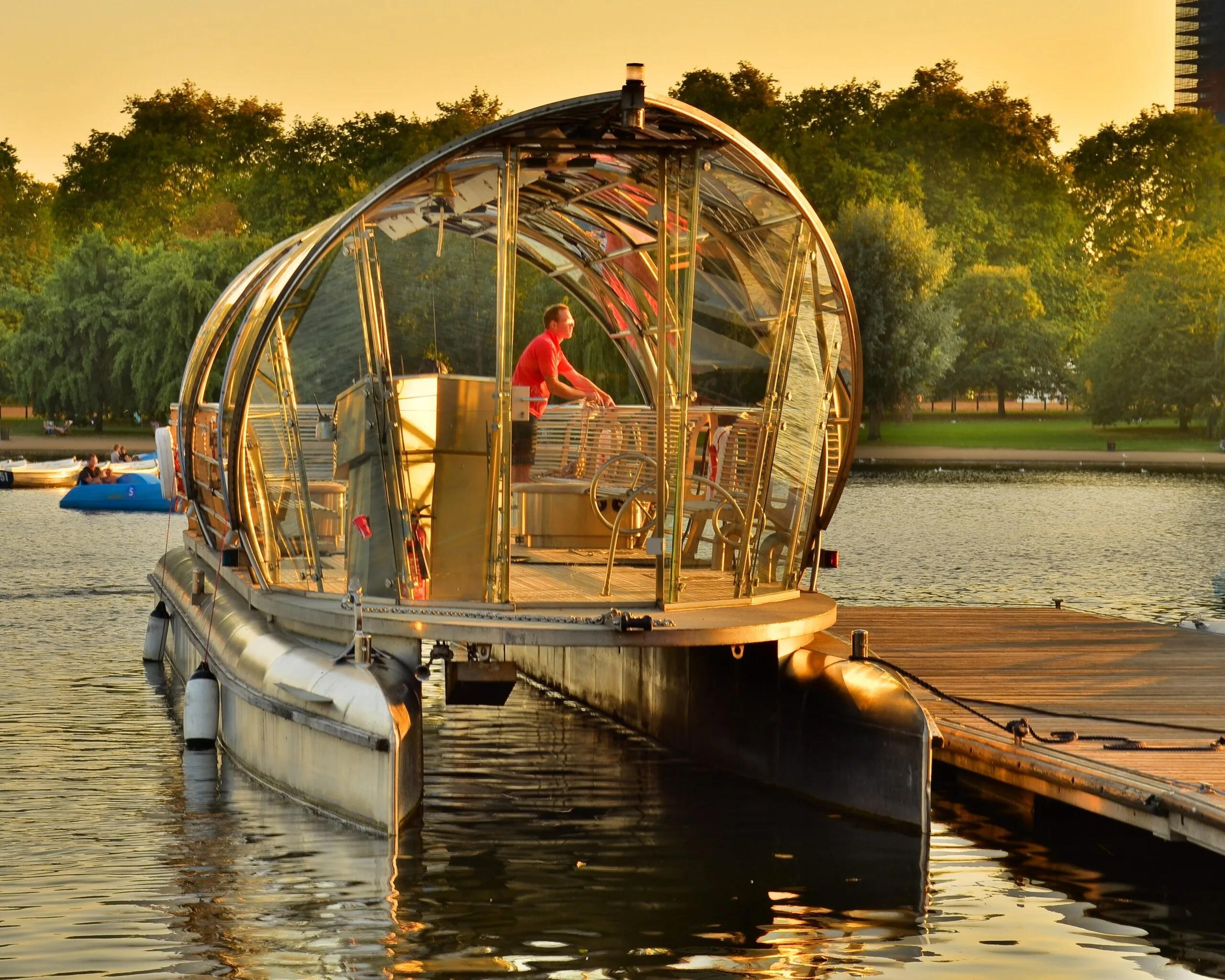 The Serpentine Solar Shuttle, a curved glass-roofed solar boat, on the lake in Hyde Park