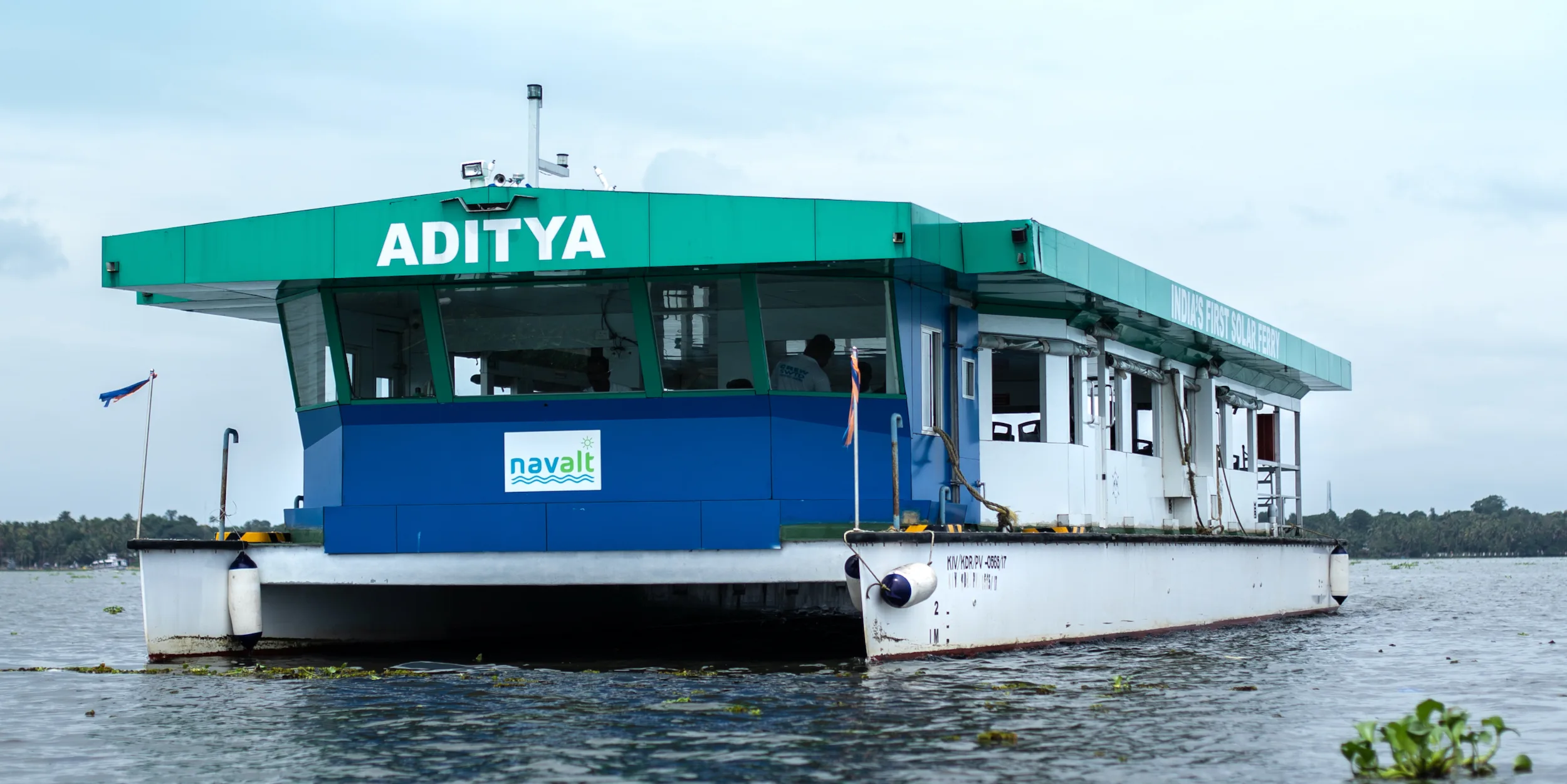 The Aditya solar ferry, a blue and white catamaran with a large solar roof, moored in Kerala