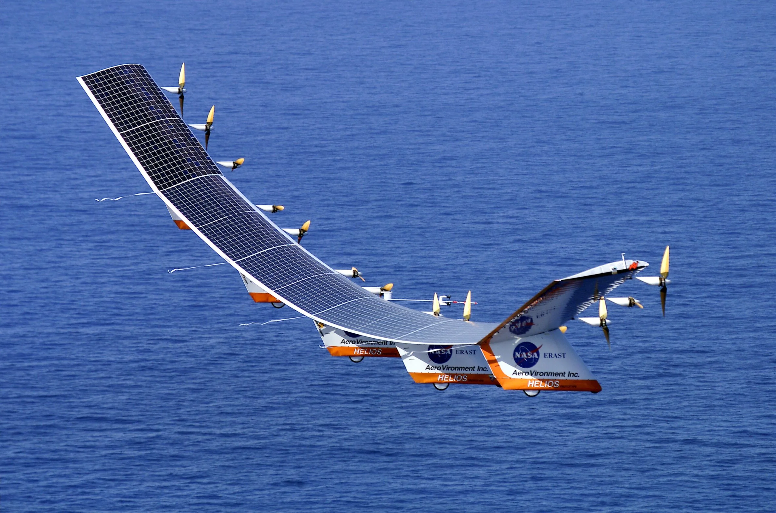NASA Helios Prototype, a long white flying wing covered in solar cells, flying over the Pacific Ocean