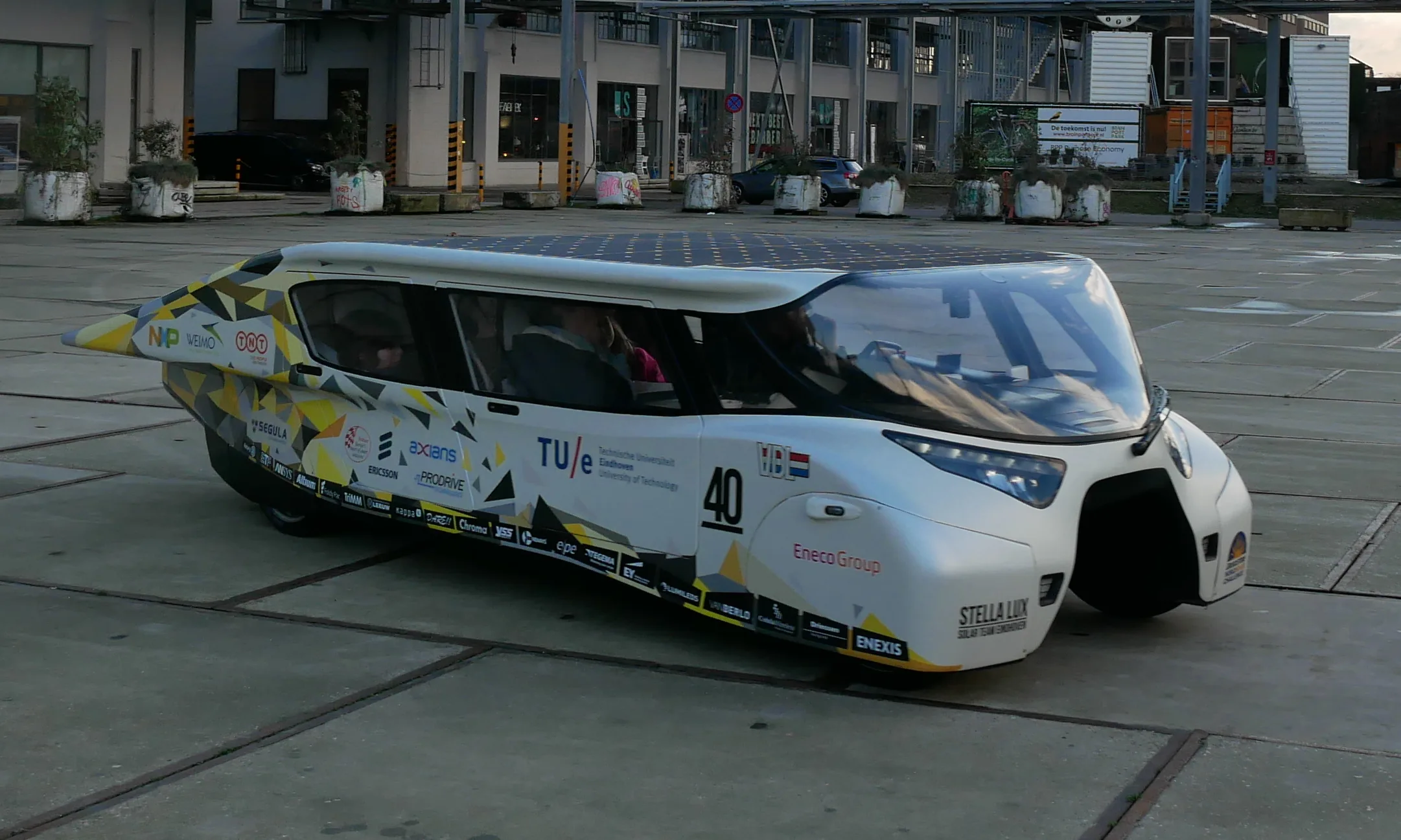 Stella Lux, a white four-seat solar family car, parked on a city square
