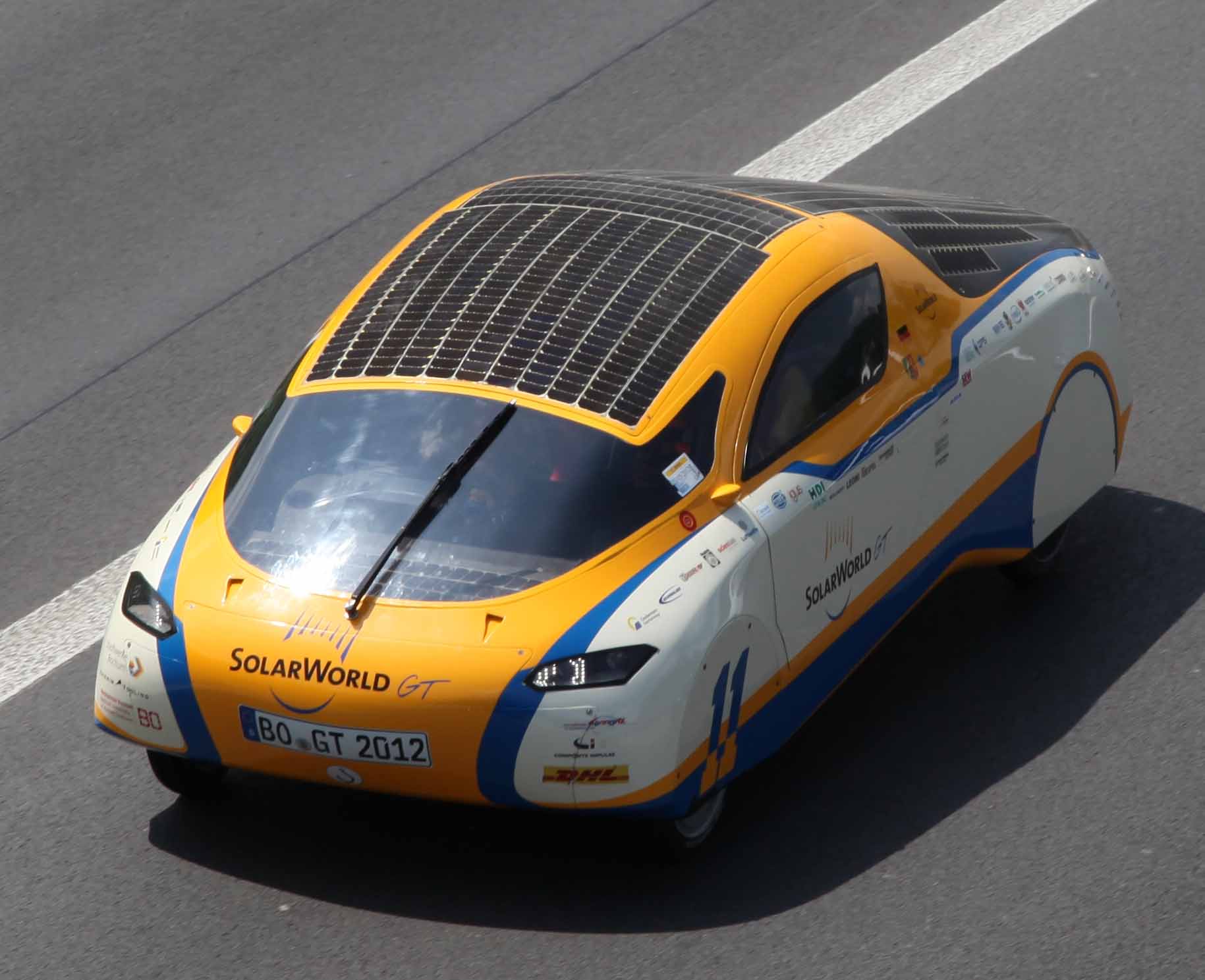 The yellow and white SolarWorld GT solar car with its solar roof driving on a road