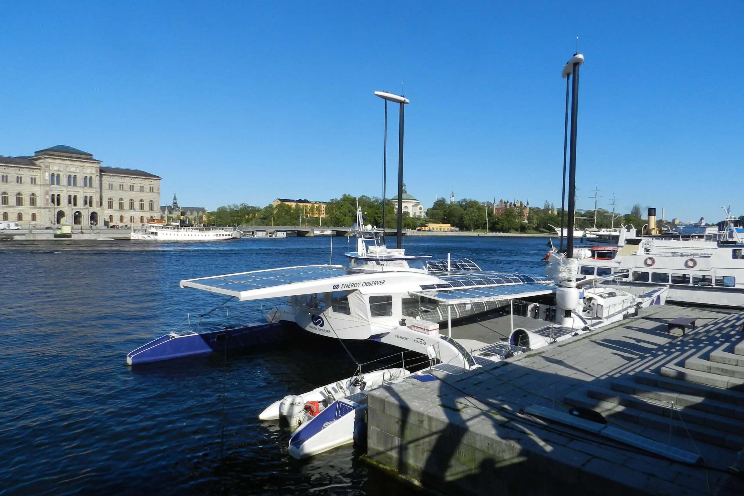 Energy Observer catamaran moored in Stockholm, its deck covered with solar panels
