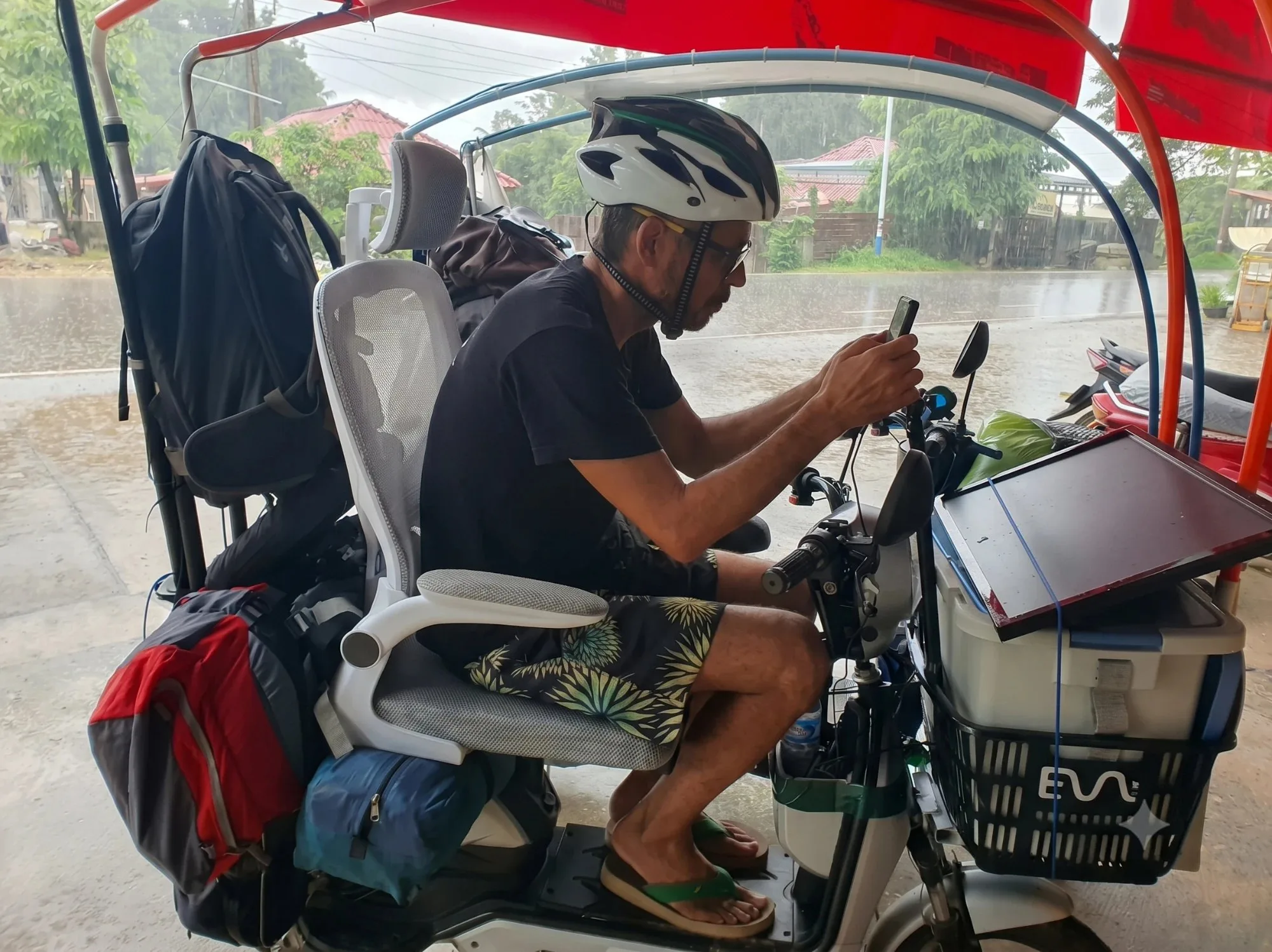 Florian Prensena on a Sola.Bike with a solar panel on the front basket, waiting out the rain on a trip through Laos